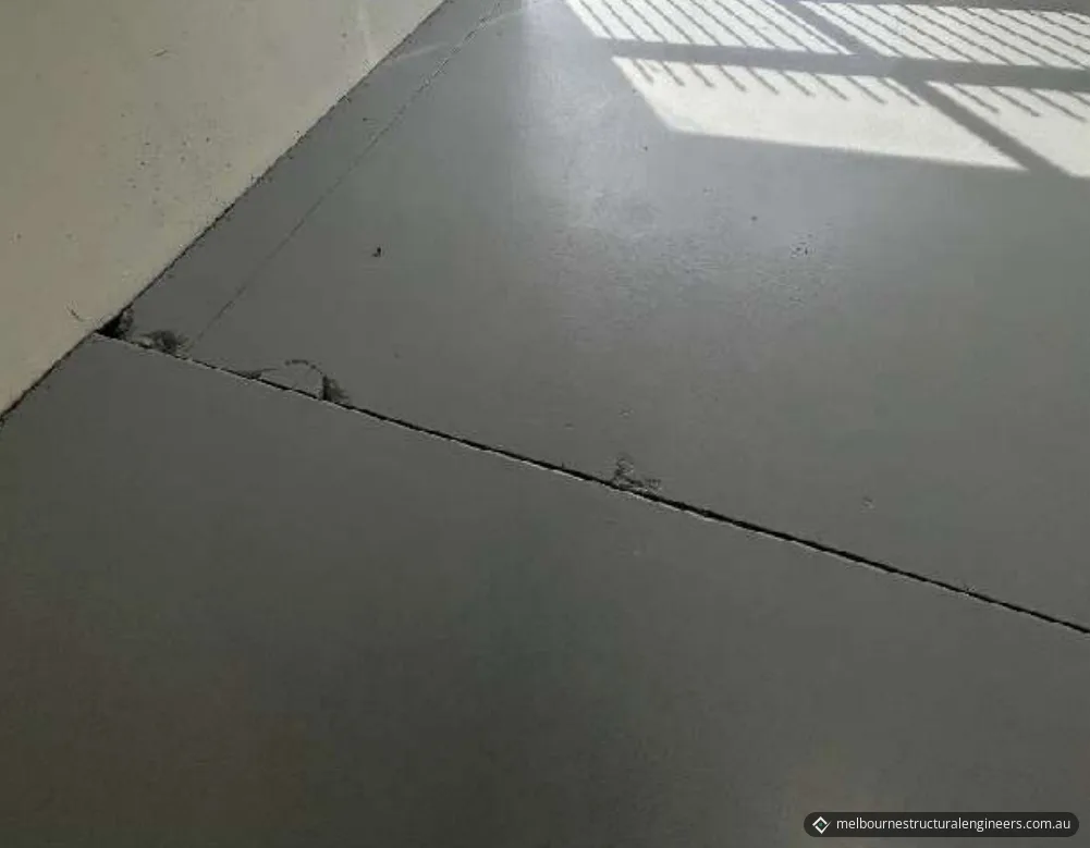A painted concrete floor with a crack line and small areas of damaged concrete running towards a wall