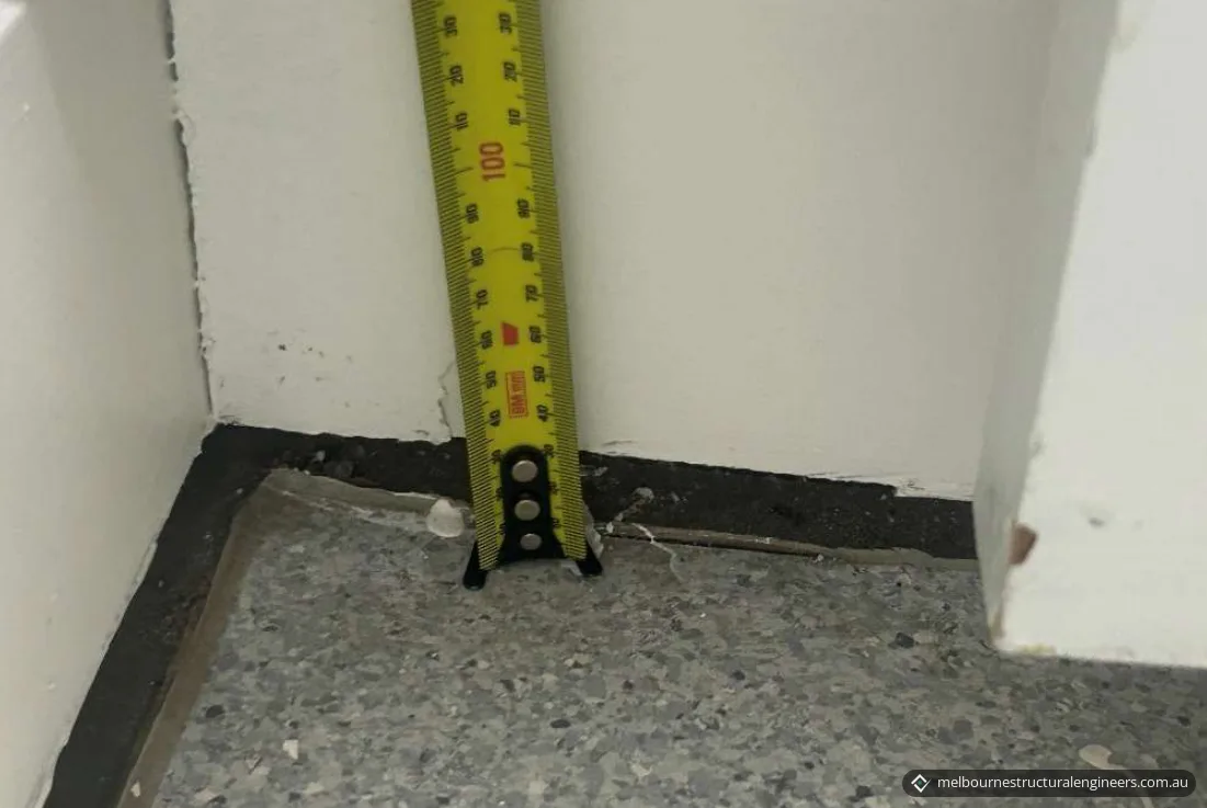 A tape measure at the base of a wall where a dark gap runs between the wall and the floor finish