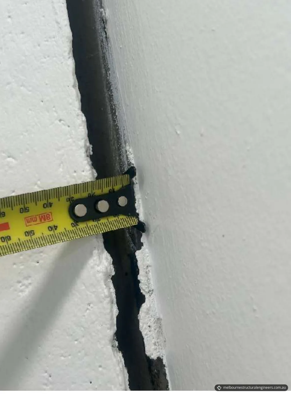 A tape measure held across a wide vertical gap between two adjoining rendered walls