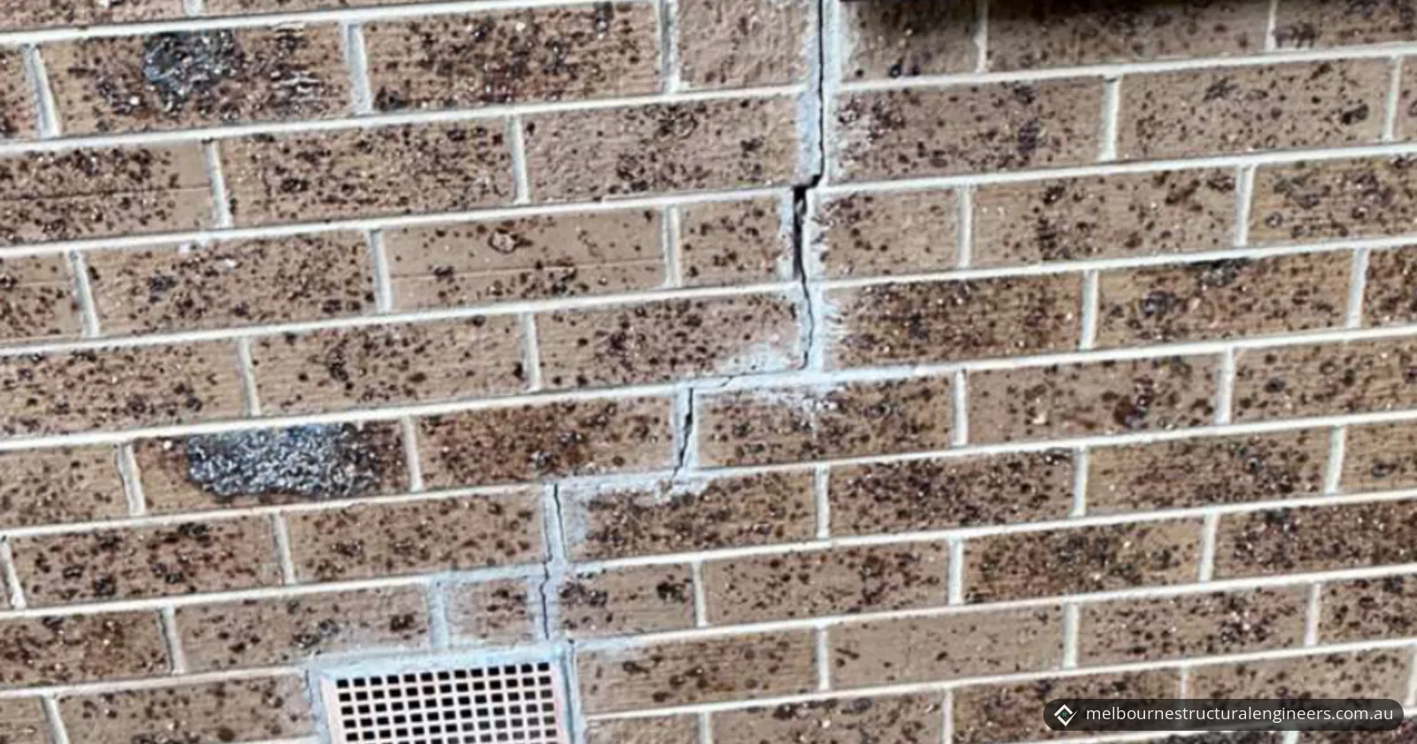 Stepped crack through the mortar joints of a face brick wall, running down towards a wall vent